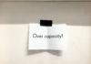 Ein Papierschild hängt an einer Tür. Darauf steht: Over capacity!