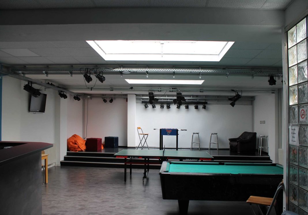 Ein Raum mit Oberlicht, im Vordergrund ein Billardtisch, dahinter eine Tischtennisplatte, dahinter auf einem Podest ein Kicker und ein braunes Ledersofa.