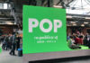 Ein großer grüner Würfel mit der Aufschrift POP, darunter „re:publica 2018, Berlin, May 2-4“. Daneben am Würfel angelehnt sitzt ein Mann mit Laptop auf dem Schoß.