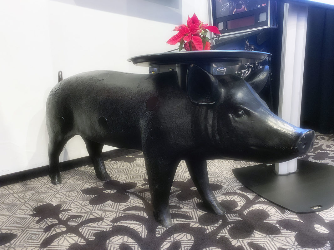 Ein großes schwarzes Deko-Schwein mit Platte auf dem Kopf, auf der wiederum ein kleiner Topf mit roten Blumen steht.