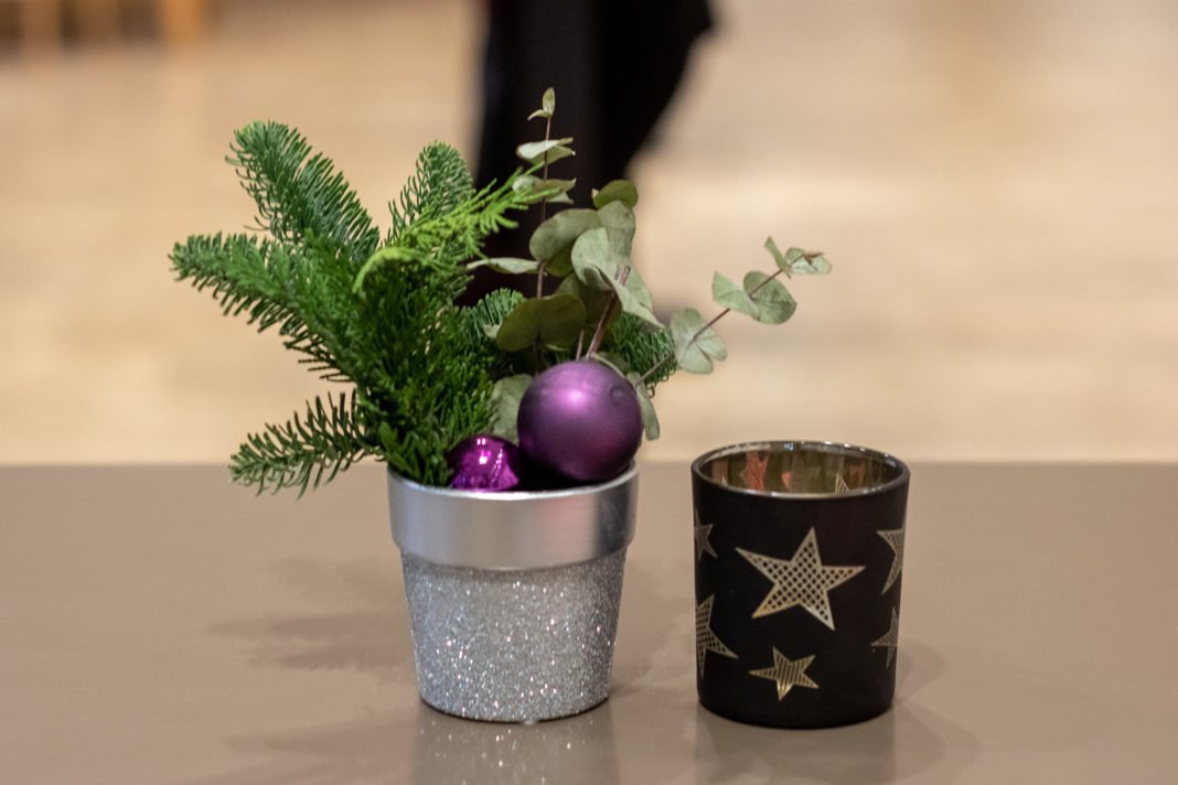 Ein kleiner Topf mit Nadelbaumzweig und Weihnachtsbaumkugel, daneben ein Teelichtbehältnis mit Stern darauf
