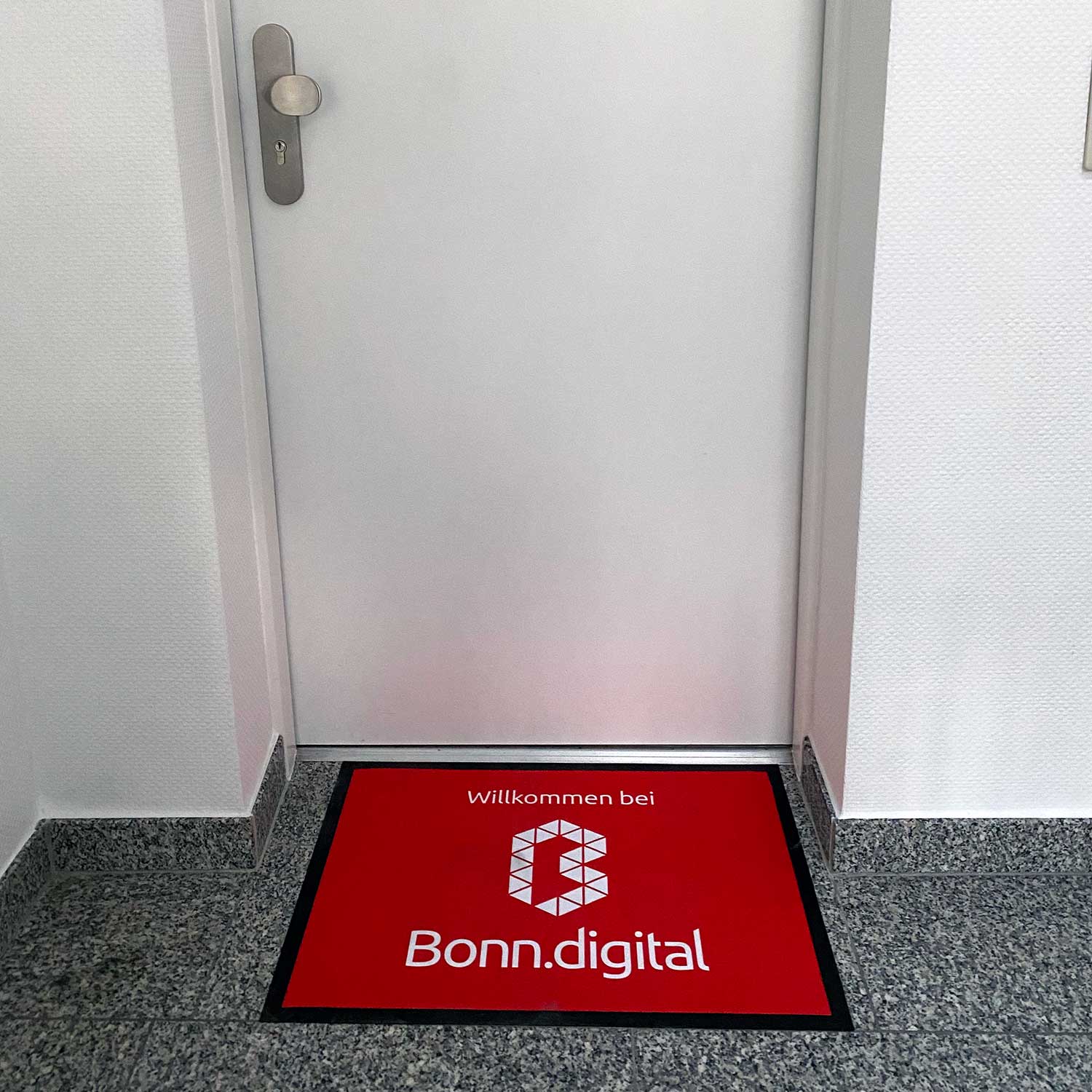 Eine rote Fußmatte mit weißem Aufdruck „Willkommen bei Bonn.digital“