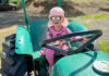 Die Tochter sitzt auf einem alten Traktor, hält das Lenkrad in der Hand und freut sich