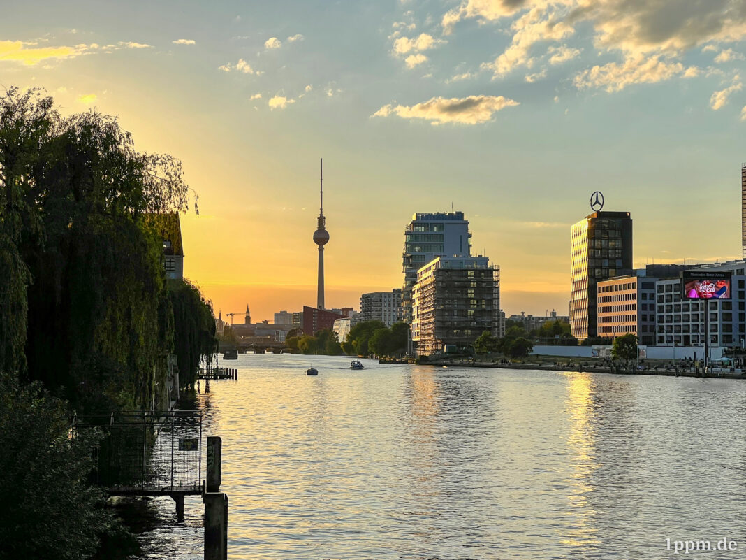 Berliner Panorama mit Fernsehturm am Horizont und Spree vorne, alles bei untergehender Sonne.