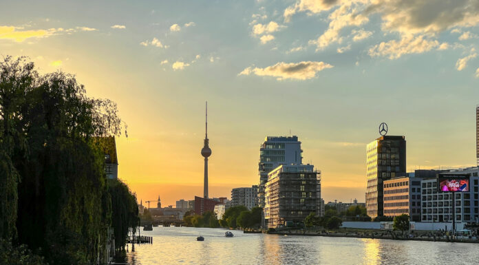 Berliner Panorama mit Fernsehturm am Horizont und Spree vorne, alles bei untergehender Sonne.