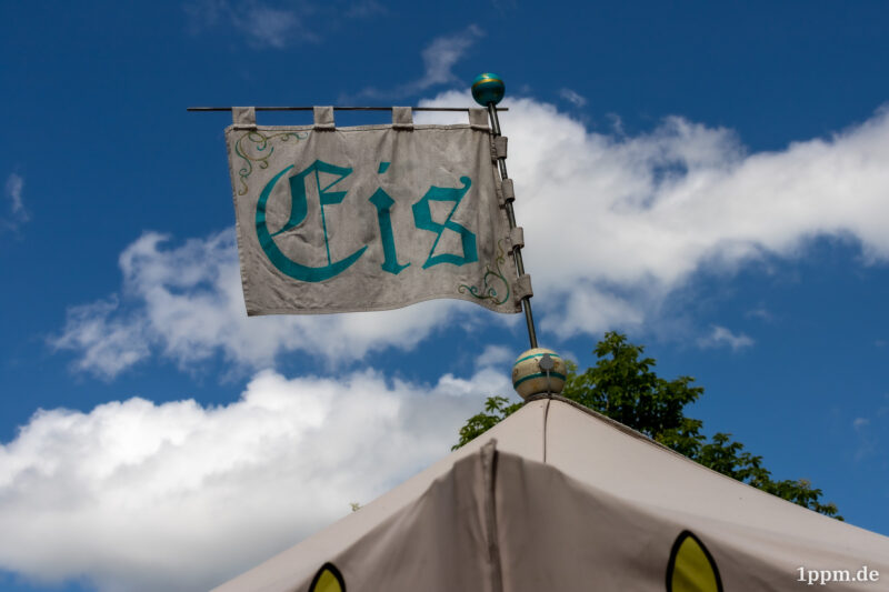 Eine Fahne auf einem Zelt, auf der etwas verschnörkelt „Eis“ steht.