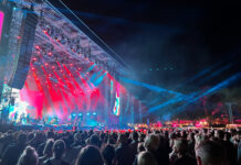 Eine Bühne von schräg links mit rot-blau leuchtenden Scheinwerfern, davor viele, viele Menschen