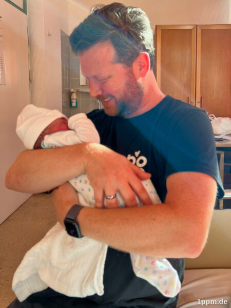 Johannes hält ein Baby auf dem Arm und lächelt selig