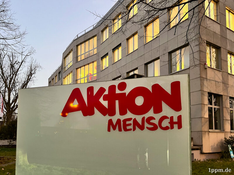 Schild vor dem Gebäude der Aktion Mensch mit deren Logo.