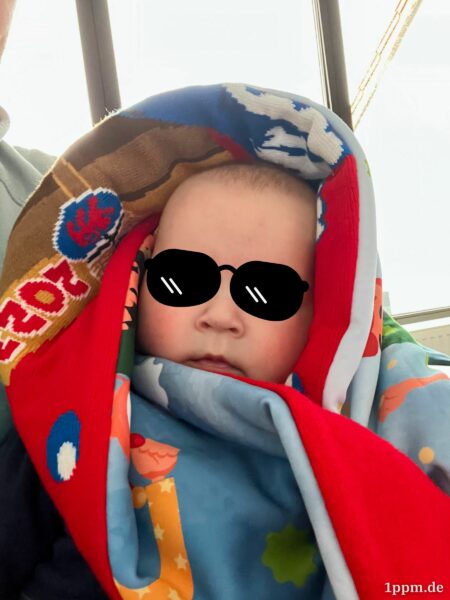 Ein kleiner Junge ist in einen Schal gewickelt. Auf seine Augen wurde eine Sonnenbrille retuschiert.