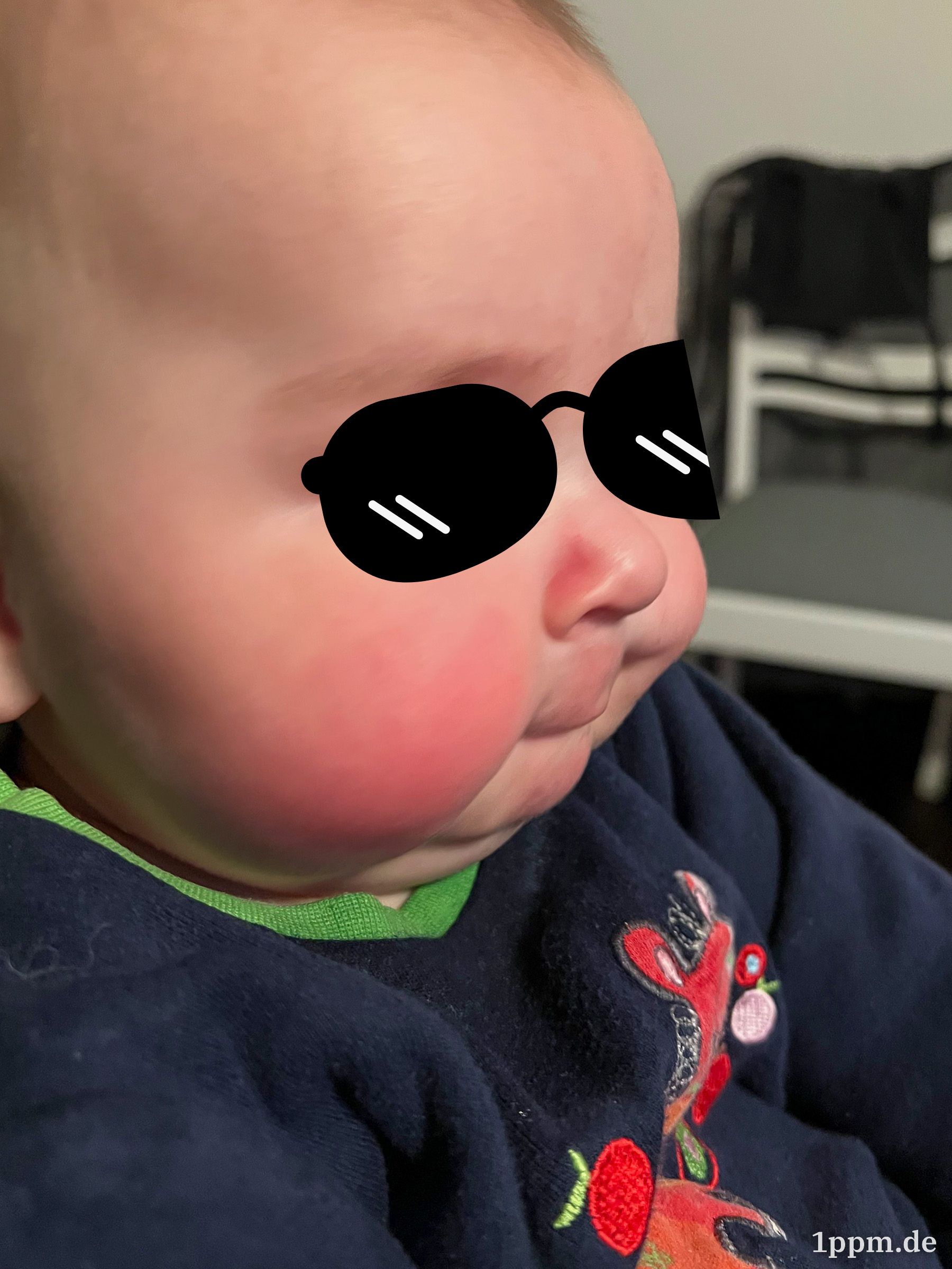 Ein Junge mit recht dicken, roten Backen. Auf seine Augen ist eine Sonnenbrille retuschiert.