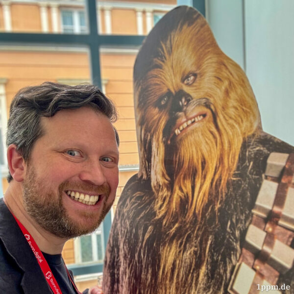 Ein grinsender Johannes links, daneben ein Pappaufsteller von Chewbacca, einem sehr haarigen Wesen.