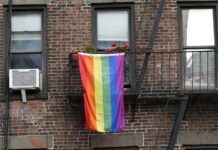 Eine Regenbogenflagge, die aus einem Fenster eines braun geziegelten Hauses hängt.