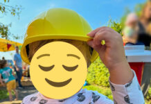 Ein Kleinkind setzt sich gerade einen gelben Bauarbeiterhelm auf. Das Gesicht ist mit einem 😌-Emoji unkenntlich gemacht.