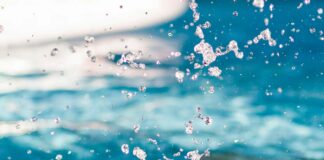 Man erahnt ein Schwimmbecken und sieht eine Person, die fast vollständig unter Wasser ist. Es spritzt viel.