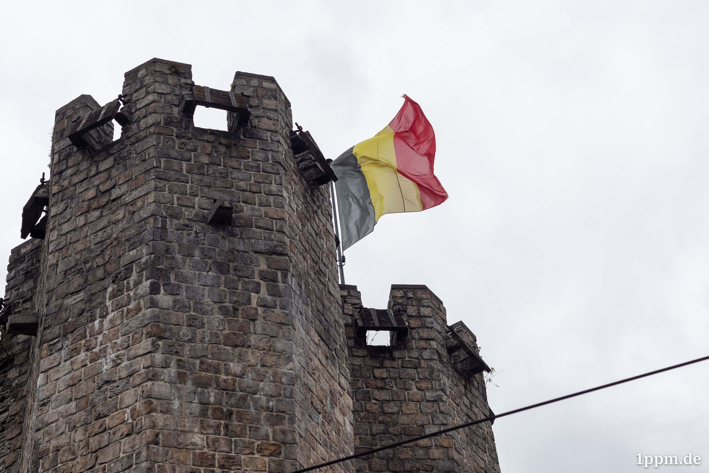 Ein Burgturm mit einer belgischen Flagge von unten fotografiert.