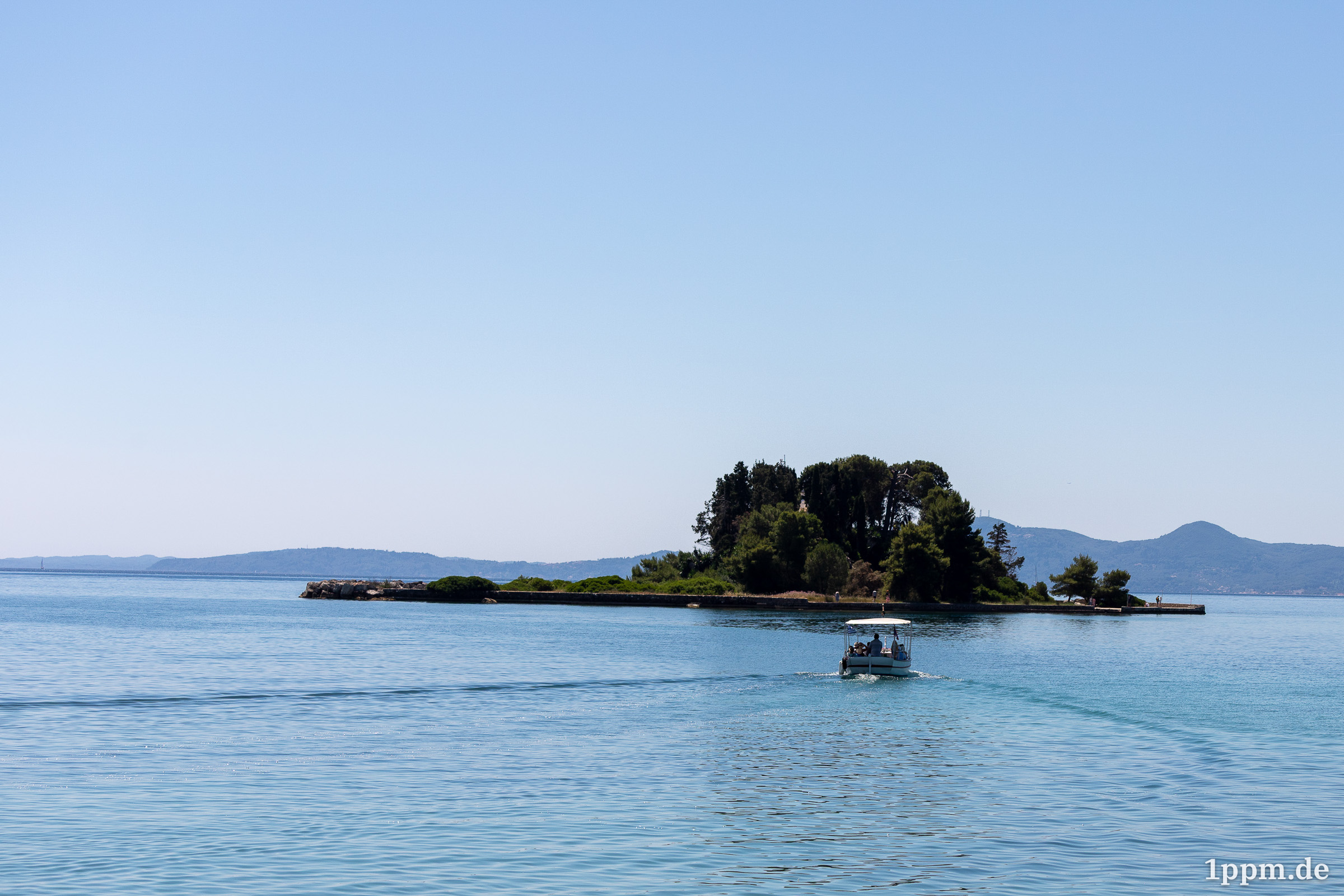 Eine kleine Insel mit ein paar Bäumen darauf, davor ein Boot mit ein paar Menschen, das Kurs auf die Insel nimmt.