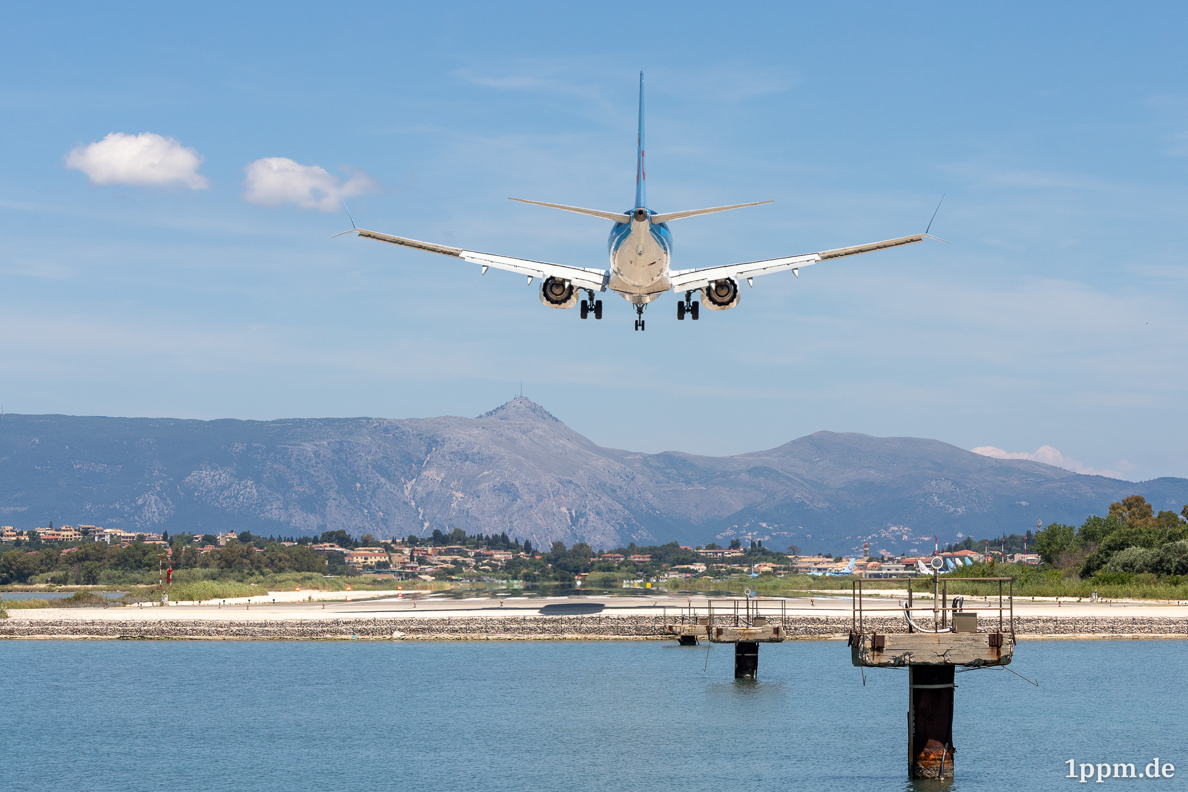 Ein Flugzeug von hinten, es ist nur noch wenige Meter über der Landebahn. Im Hintergrund erkennt man halbhohe Berge.