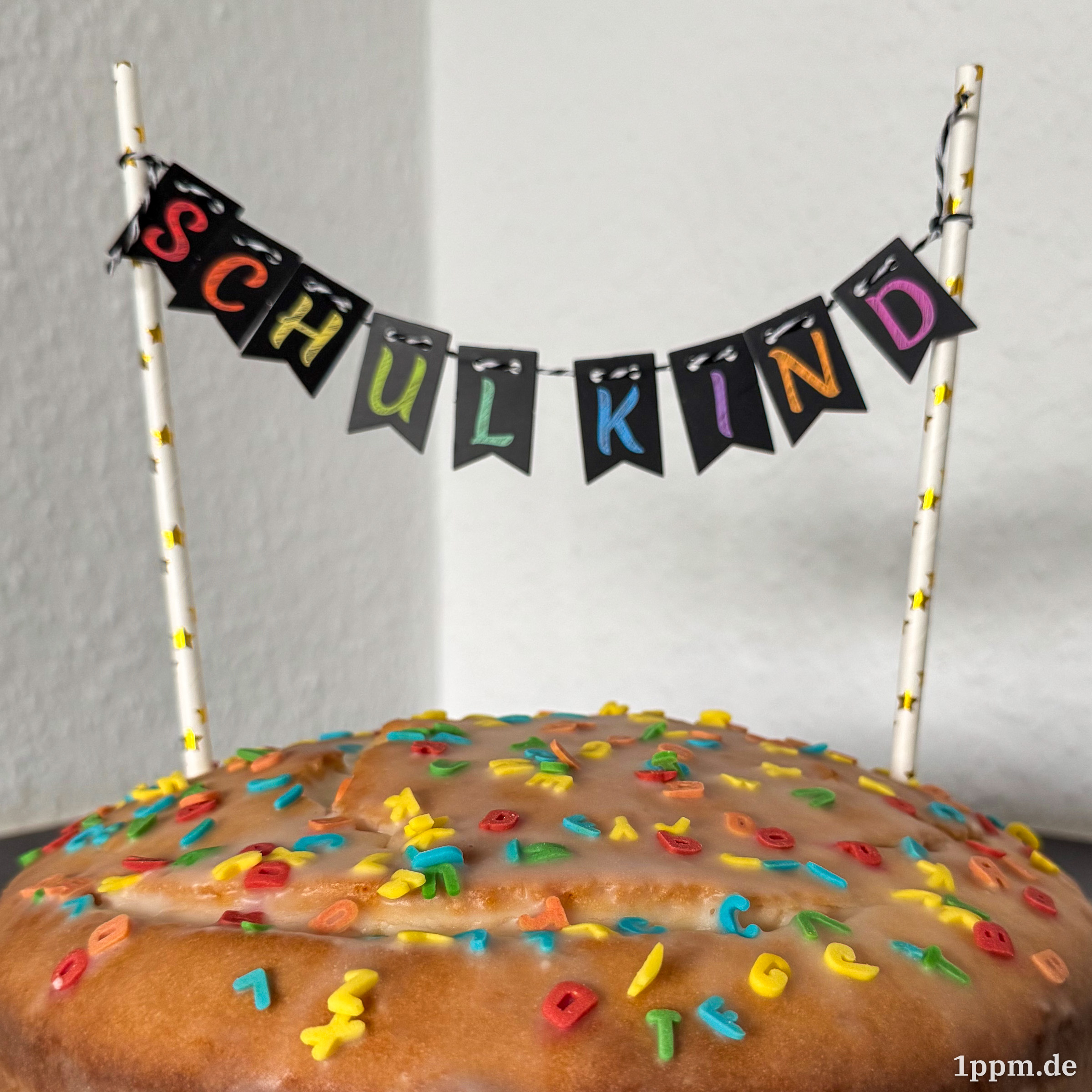 Ein Kuchen voller kleiner Zuckerbuchstaben und einer Wimpelkette darüber, die „Schulkind“ zeigt