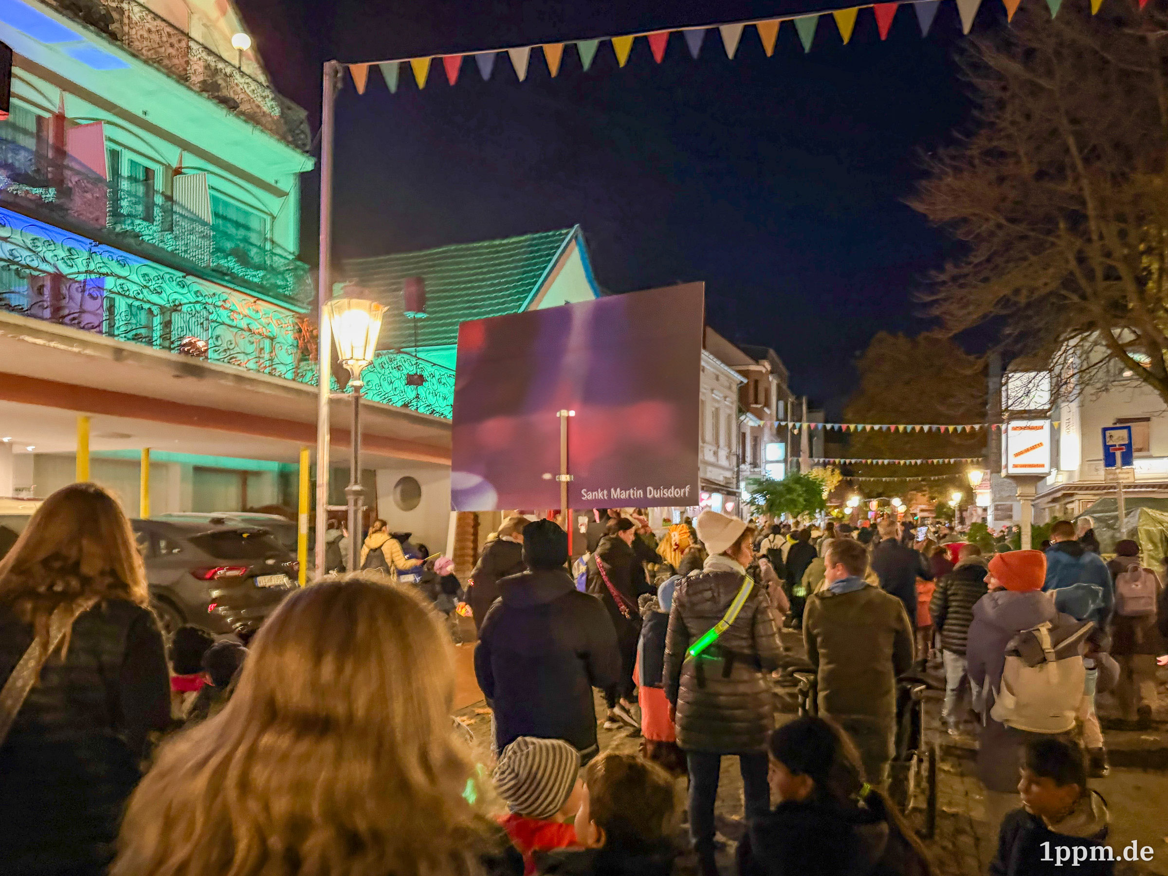 Viele Menschen von hinten, es ist dunkel. In der Bildmitte ein Schild, auf dem "Sankt Martin Duisdorf" steht.