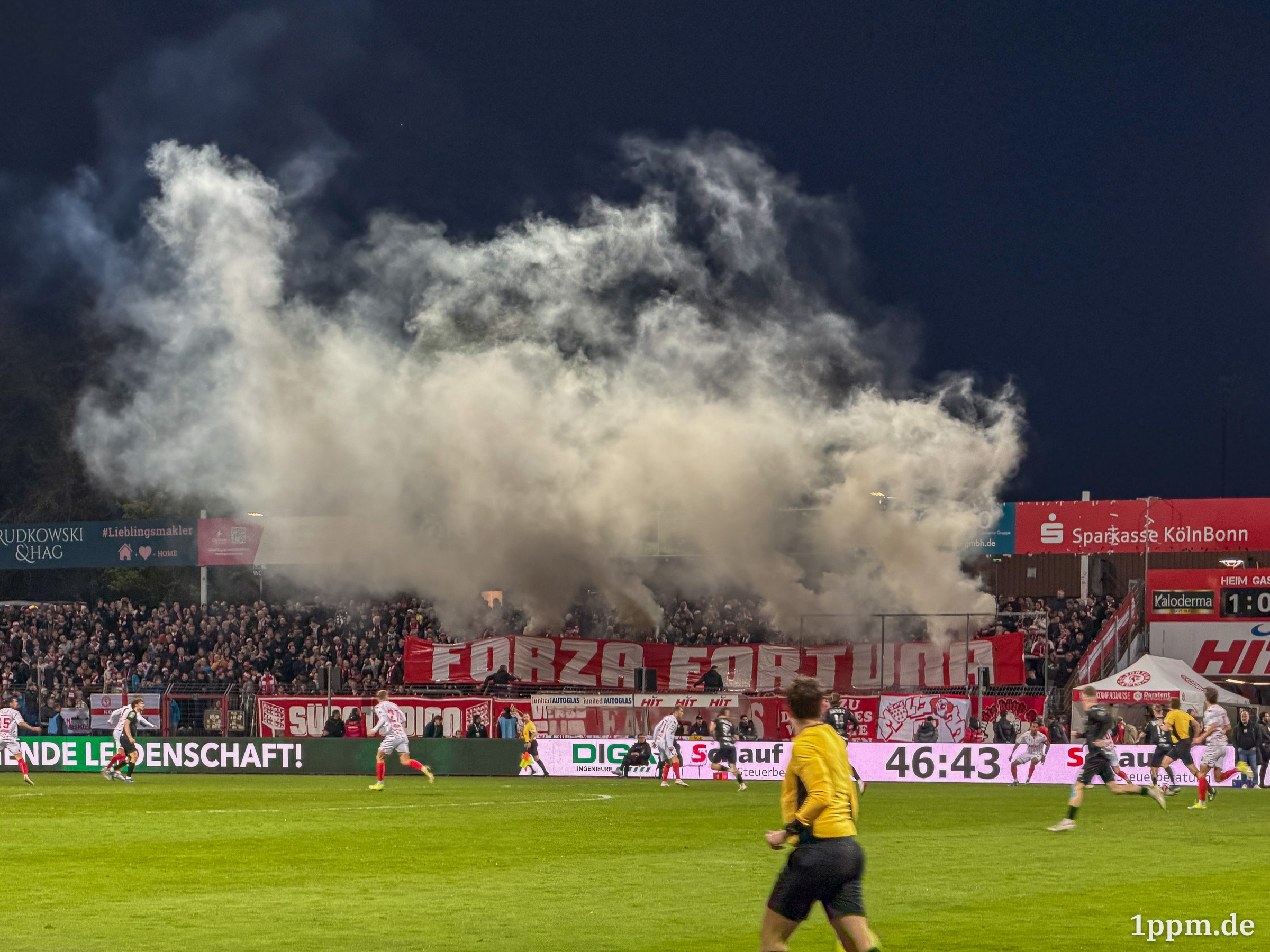 Fußballstadion mit Spielern auf dem Spielfeld und einer großen Rauchwolke über den Zuschauerrängen