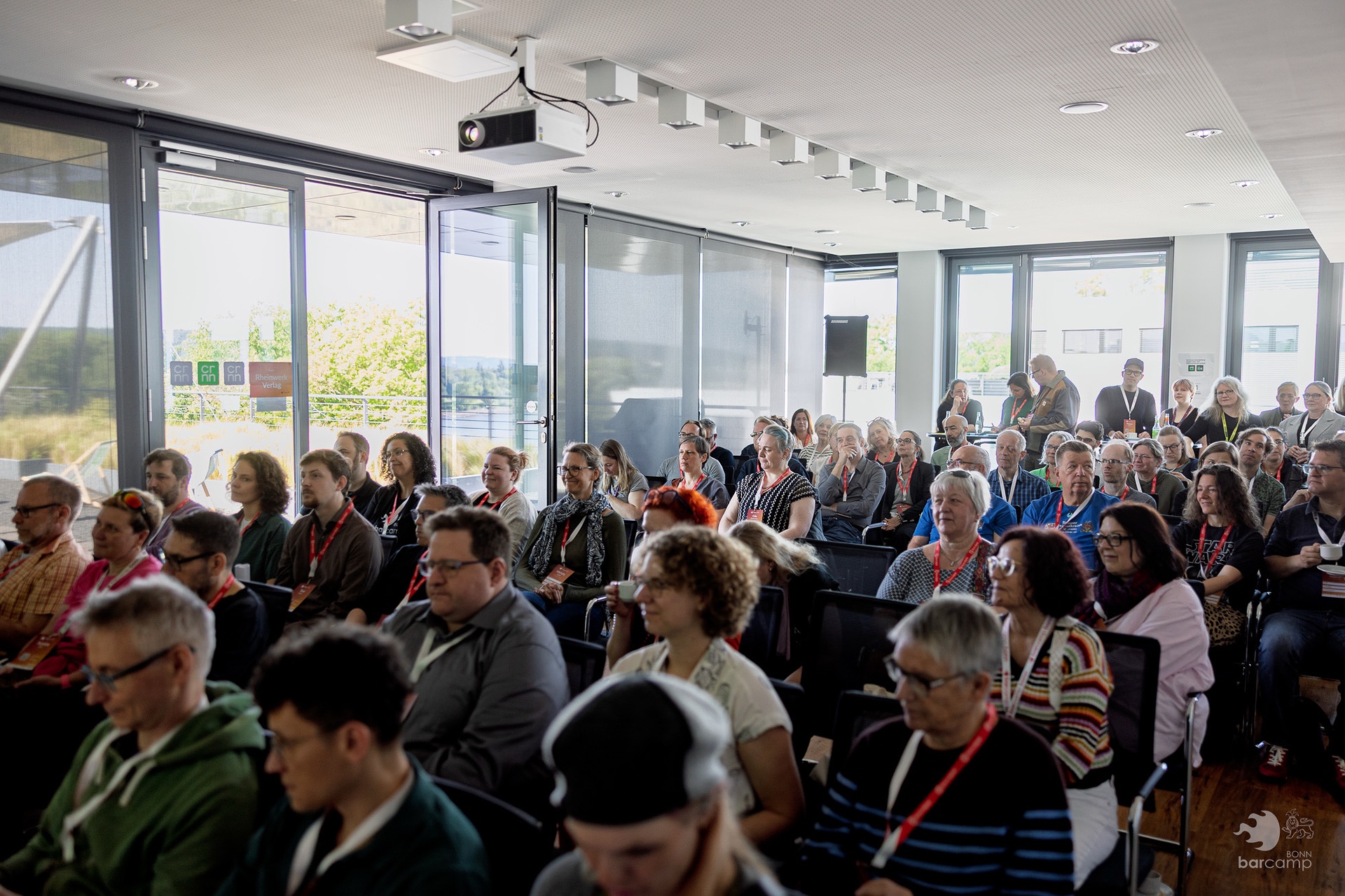 Publikum in einem hellen Konferenzraum mit großen Fenstern, sitzend und nach vorne blickend