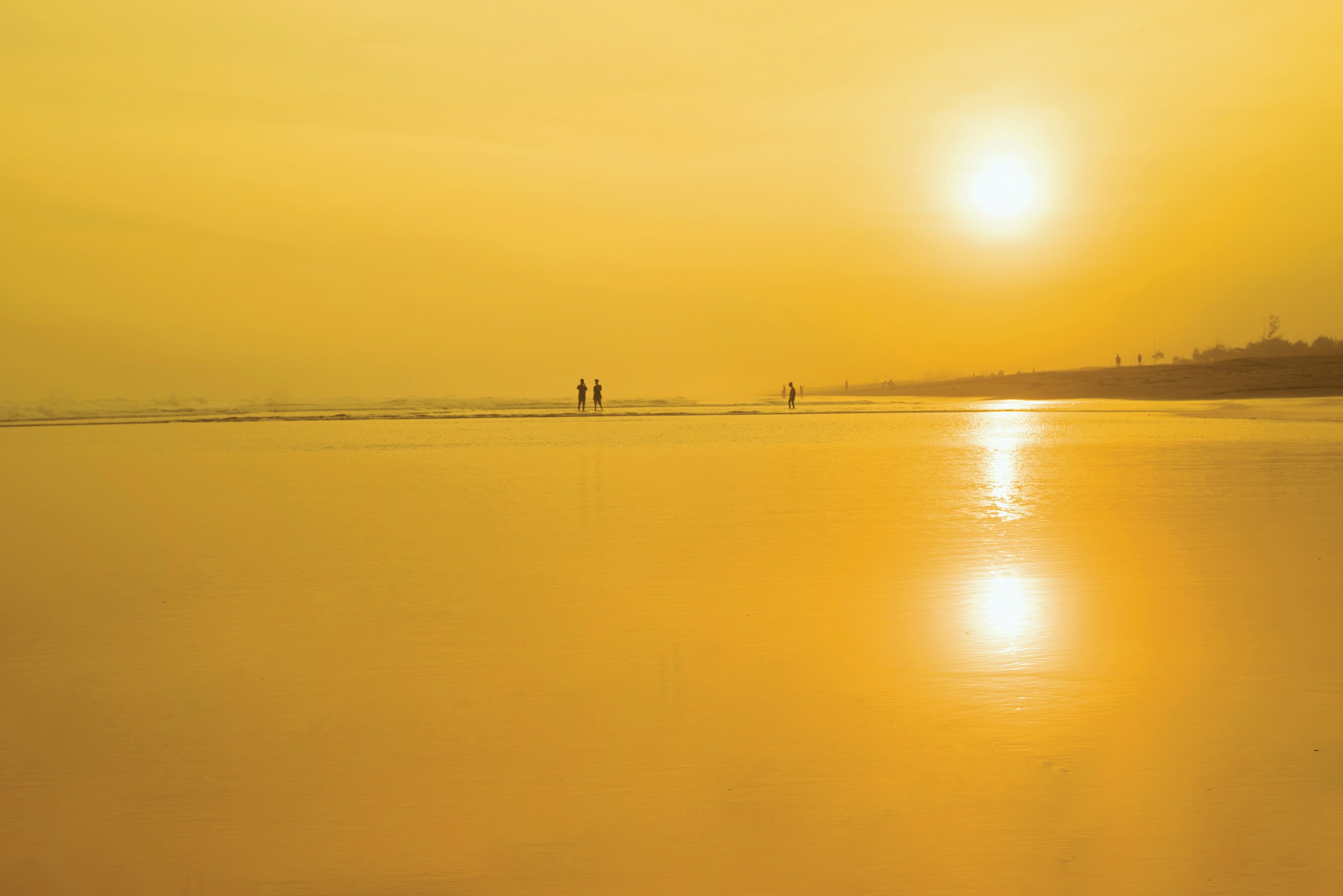 Strand mit spiegelndem Wasser und zwei Personen in der Ferne bei Sonnenuntergang
