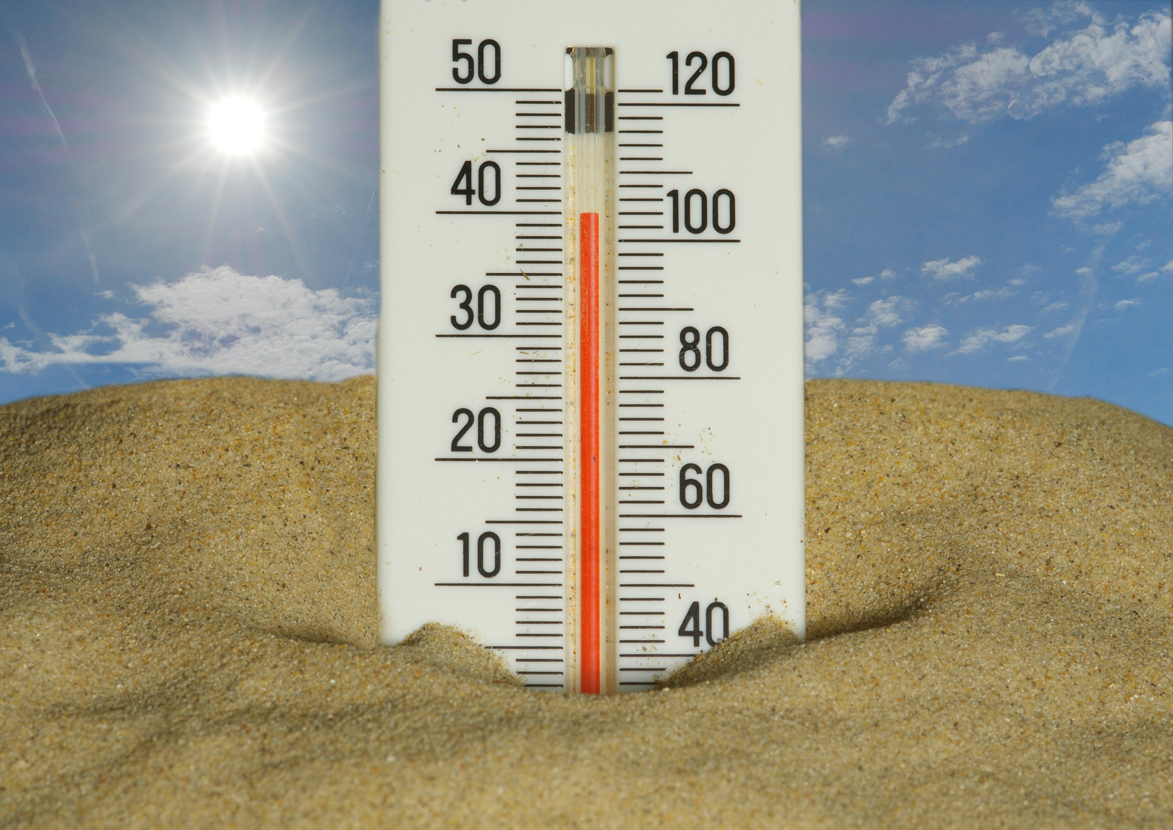 Thermometer im Sand mit Sonnenschein und blauem Himmel im Hintergrund