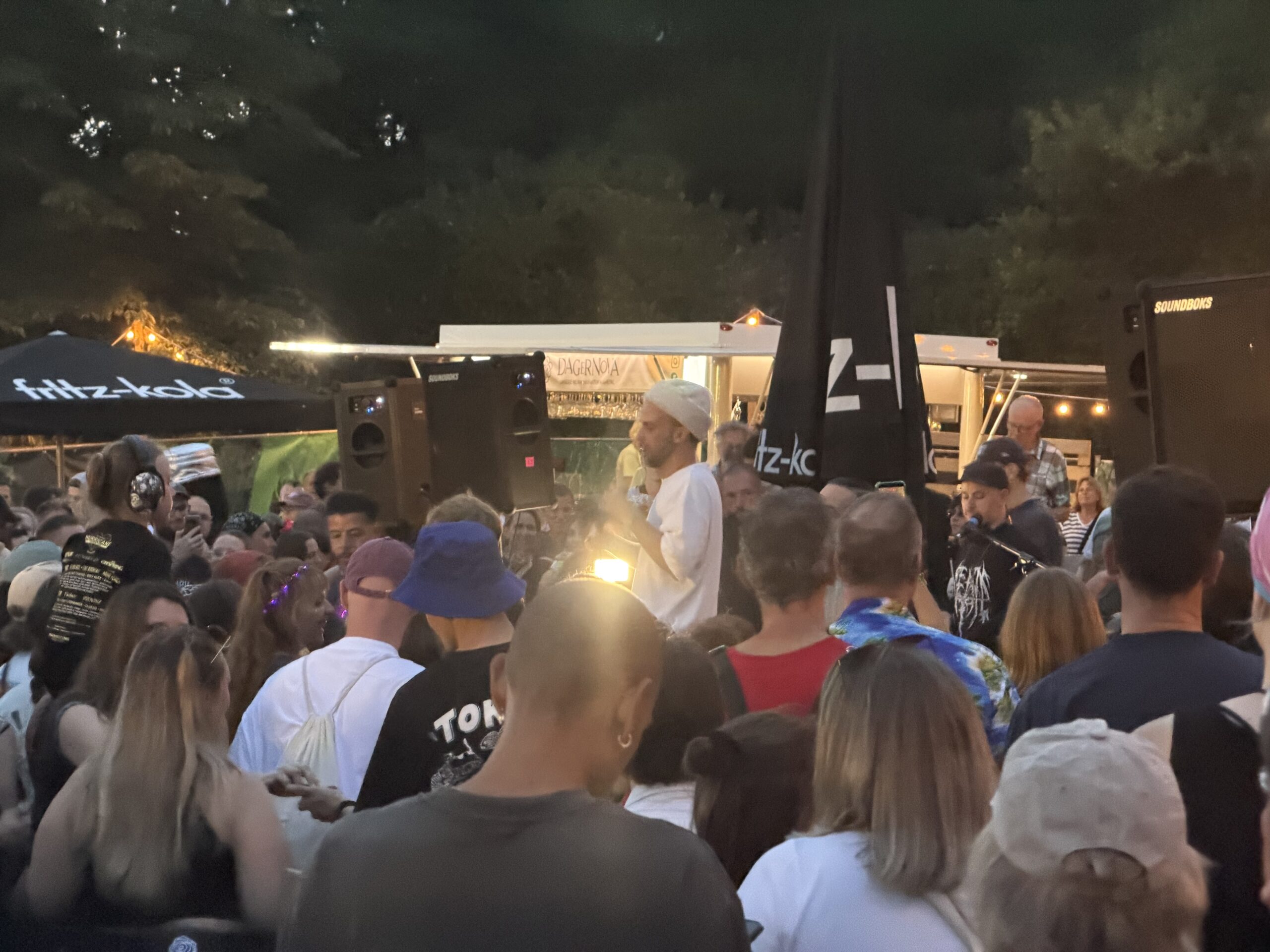 Menschenmenge bei einer Open-Air-Veranstaltung mit einem Mann in weißem T-Shirt und weißer Mütze, der in der Mitte steht